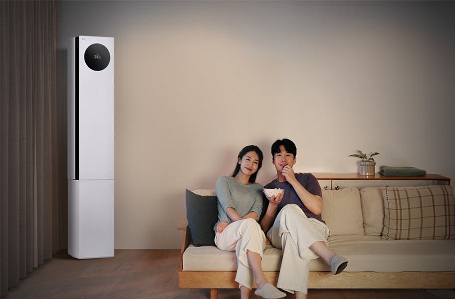 LG 휘센 AI 오브제컬렉션 뷰I 프로 에어컨이 왼쪽에 세워져 있으며, 원형 디스플레이에는 24.5℃라는 숫자가 표시되어 있습니다. 오른쪽에는 소파에 앉아 있는 두 사람이 보이며, 남성은 팝콘을 들고 있습니다. 소파 뒤쪽에는 수납장이 놓여 있고 그 위에는 식물과 수건이 놓여 있습니다.