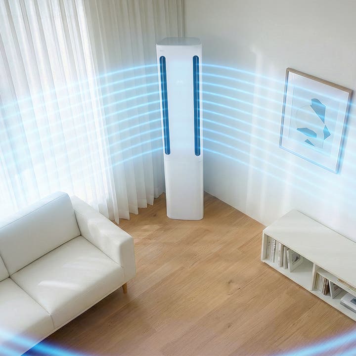 거실 중앙에 세워진 LG 휘센 AI 오브제컬렉션 쿨 에어컨이 보입니다. 에어컨 상단의  디지털 디스플레이에 온도 정보가 표시되어 있습니다. 에어컨 양쪽으로 연한 파란색 선 형태의 그래픽이 사방으로 퍼져 벽면을 따라 시원한 공기가 흘러 나가는 모습으로, 공간 전체를 냉방해주는 모습이 시각적으로 표현되어 있습니다. 왼쪽에는 큰 창문을 통해 자연광이 들어오고, 창가 앞에는 밝은 색의 2인용 소파가 배치되어 있으며, 오른쪽 벽에는 액자가 걸려 있고 1단 수납장과 탁상용 조명이 놓여 있습니다. 이 이미지는 에어컨 양쪽 토출구를 통해 강력한 바람이 나오는 실내 공간을 시각적으로 표현하고 있습니다.