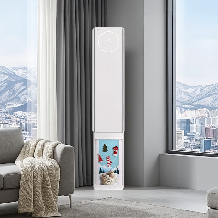 전체적으로 겨울 느낌이 나는 인테리어컷으로 에어컨은 중앙에 놓여져 있고 뷰케이스에는 눈사람, 트리, 산타클로스 모자, 양말 등의 오브제가 걸려 있는 장식품이 놓여져 있습니다. 양쪽 창밖으로는 눈이 덮힌 도시와 산의 전경이 보여지며, 좌측에는 담요가 걸쳐져 있는 소파가 배치되어 있으며, 우측에는 벽난로와 함께 담요가 걸쳐져 있는 수툴이 배치되어 있습니다. 