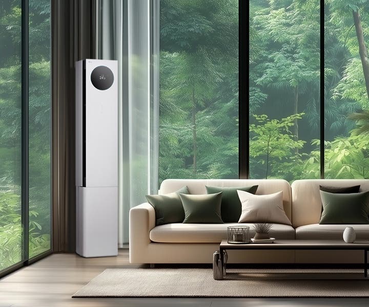 LG 휘센 AI 오브제컬렉션 뷰I 프로 에어컨이 거실의 왼쪽 구석에 세워져 있으며, 에어컨의 원형 디스플레이에는 24.5°C라는 숫자가 표시되어 있습니다. 에어컨 옆으로는 큰 창문이 있어 푸른 숲의 풍경이 보이며, 창문 앞에는 베이지색 소파가 놓여 있습니다. 소파 위에는 여러 개의 녹색과 흰색 쿠션이 배열되어 있고, 소파 앞에는 낮은 테이블이 놓여 있습니다. 테이블 위에는 장식품과 책이 놓여 있으며, 오른쪽에는 큰 화분에 심어진 녹색 식물이 배치되어 있습니다.