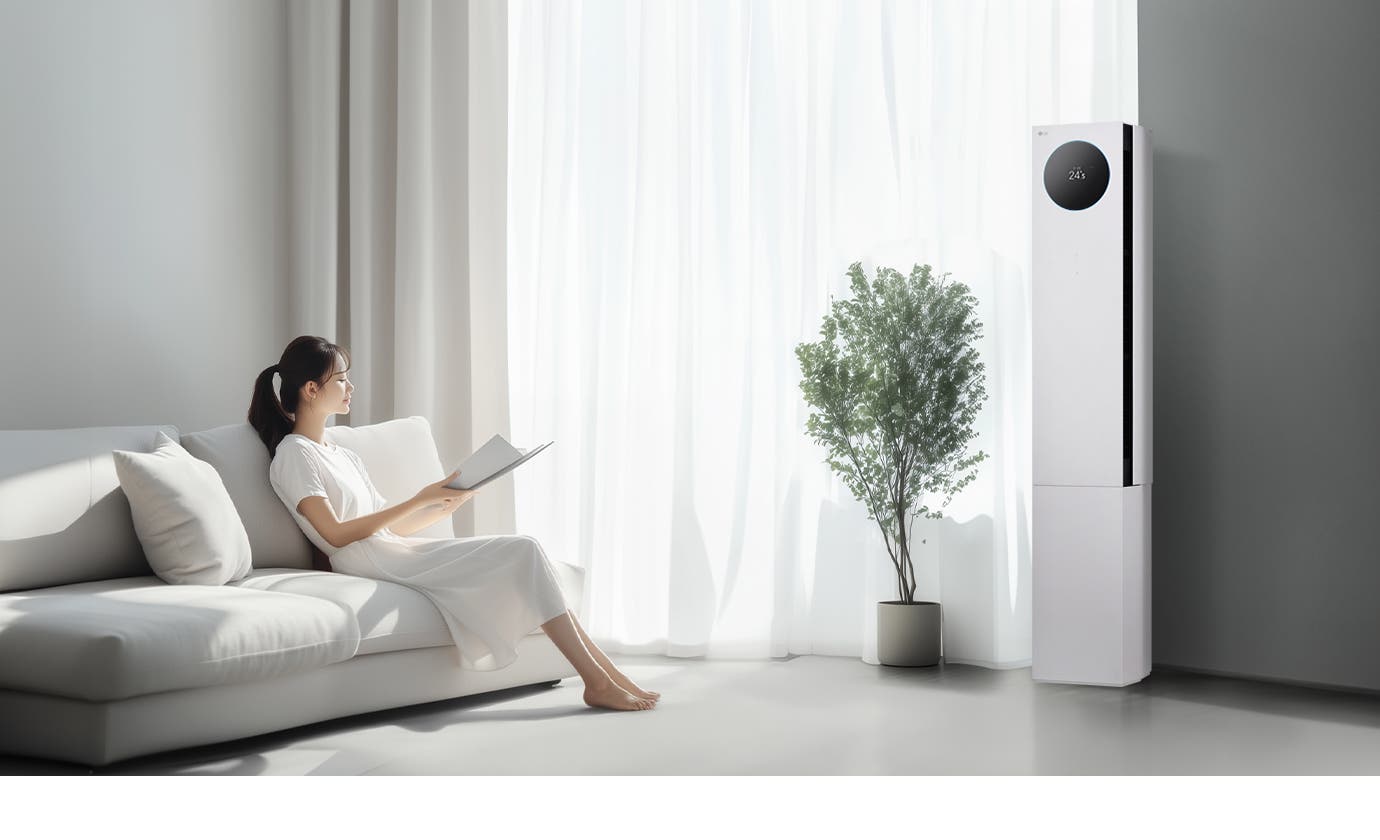 LG 휘센 AI 오브제컬렉션 뷰I 프로 에어컨이 오른쪽에 세워져 있으며, 원형 디스플레이에는 24.5°C라는 숫자가 표시되어 있습니다. 에어컨 왼쪽에는 커다란 창문이 있고, 창문을 통해 밝은 자연광이 들어오고 있습니다. 창문 앞에는 화분에 심어진 녹색 식물이 놓여 있습니다. 왼쪽에는 흰색 소파에 앉아 책을 읽고 있는 여성이 보입니다. 그녀는 흰색 원피스를 입고 있으며, 소파에는 흰색 쿠션이 놓여 있습니다.