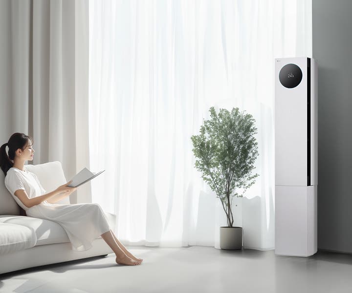 LG 휘센 AI 오브제컬렉션 뷰I 프로 에어컨이 오른쪽에 세워져 있으며, 원형 디스플레이에는 24.5°C라는 숫자가 표시되어 있습니다. 에어컨 왼쪽에는 커다란 창문이 있고, 창문을 통해 밝은 자연광이 들어오고 있습니다. 창문 앞에는 화분에 심어진 녹색 식물이 놓여 있습니다. 왼쪽에는 흰색 소파에 앉아 책을 읽고 있는 여성이 보입니다. 그녀는 흰색 원피스를 입고 있으며, 소파에는 흰색 쿠션이 놓여 있습니다.