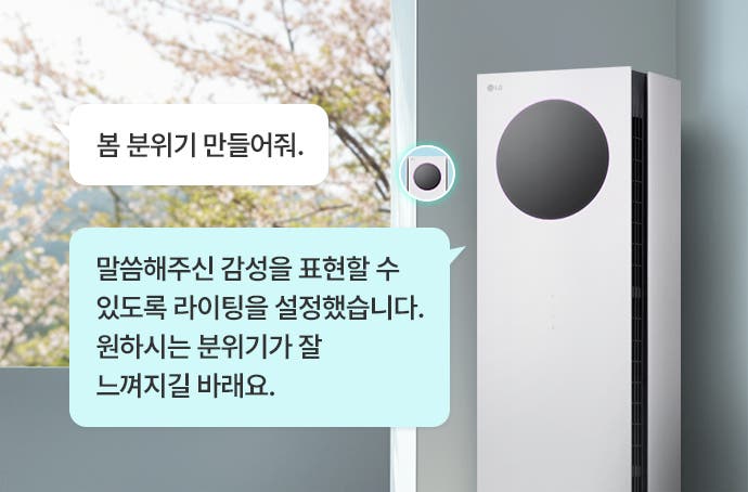 에어컨의 원형 디스플레이에는 무드라이팅이 켜져 있습니다. 화면 왼쪽에는 봄 분위기 만들어줘.라는 말풍선과 말씀해주신 감성을 표현할 수 있도록 라이팅을 설정했습니다. 원하시는 분위기가 잘 느껴지길 바래요.라는 설명이 담긴 말풍선이 있습니다. 창문 밖으로는 벚꽃이 핀 나무가 보입니다.