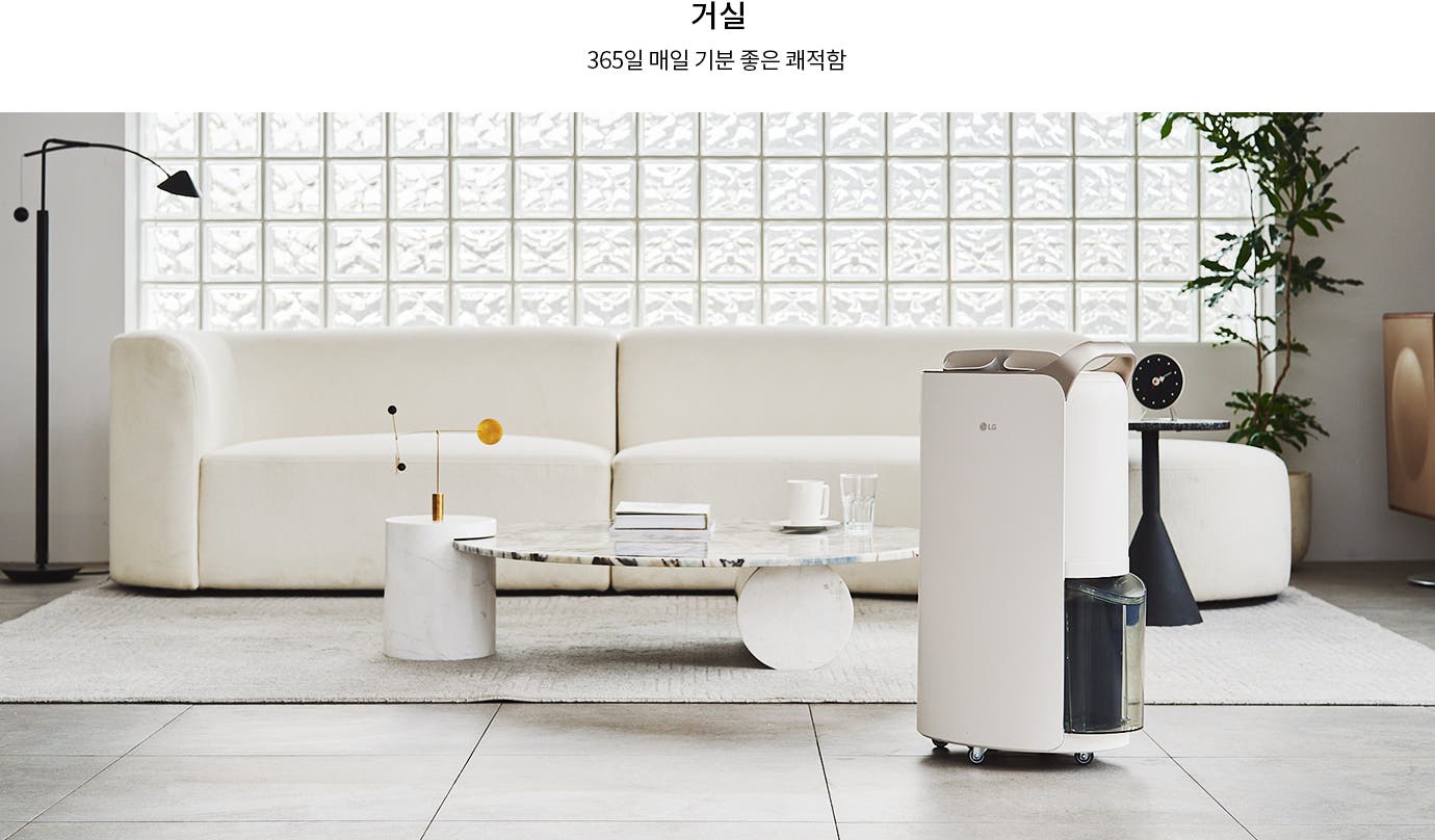 거실 공간에 흰색 소파와 대리석 테이블이 놓여 있으며, 테이블 위에는 책과 컵이 있습니다. 소파 뒤에는 유리 블록 벽이 있고, 한쪽에는 식물이 배치되어 있습니다. 바닥에는 카펫이 깔려 있으며, LG 로고가 있는 제습기가 있습니다. 상단에는 거실과 365일 매일 기분 좋은 쾌적함이라는 문구가 적혀 있습니다.