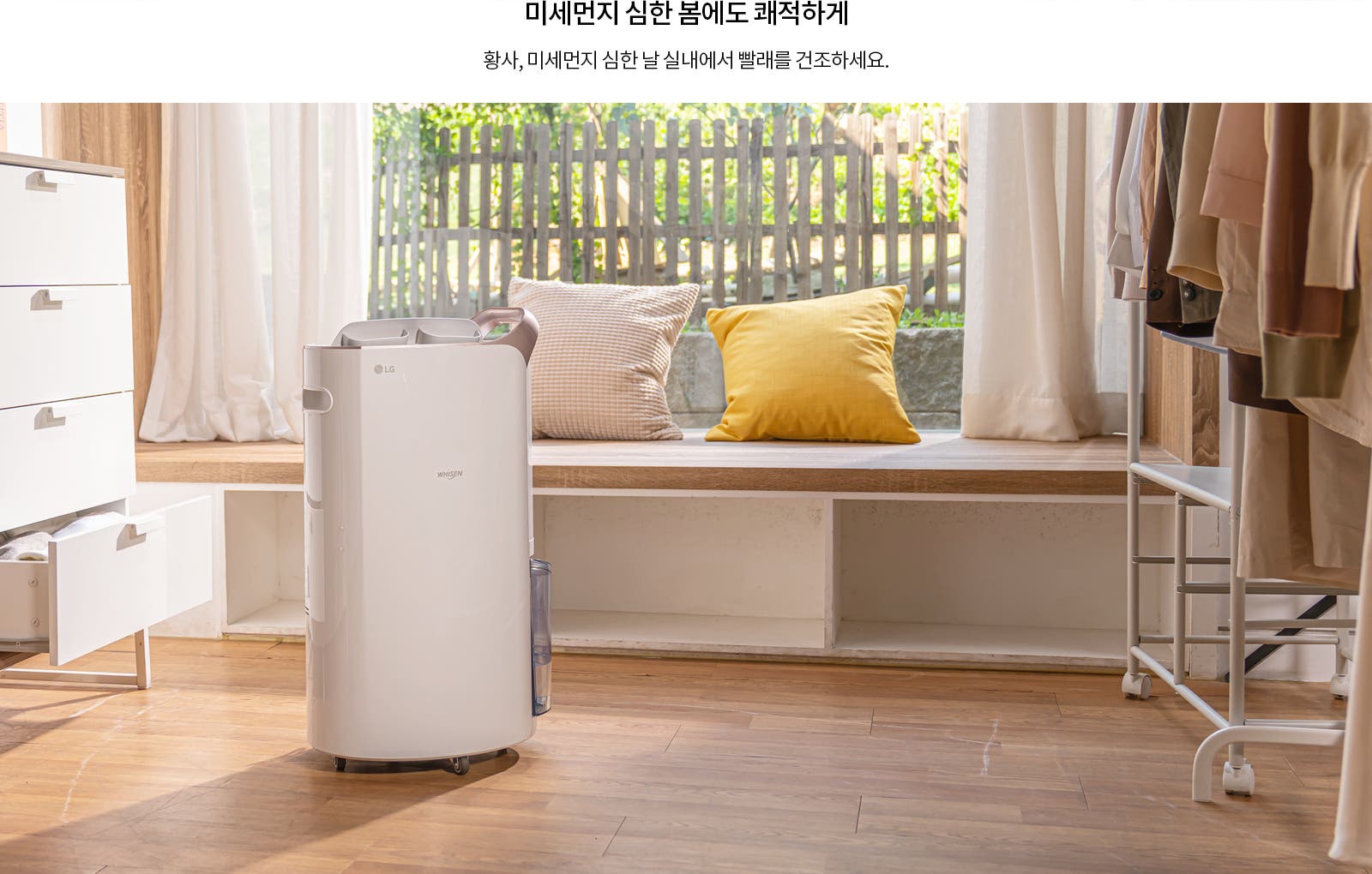 미세먼지 심한 봄에도 쾌적하게. 황사, 미세먼지 심한 날 실내에서 빨래를 건조하세요. 실내에는 LG 휘센 제습기가 놓여 있으며, 나무 바닥과 창가에 쿠션이 있는 벤치가 보입니다. 옷장에는 여러 벌의 옷이 걸려 있습니다. 창문 밖으로는 울타리와 나무가 보입니다.