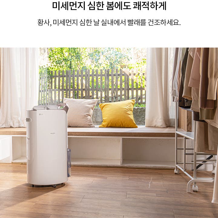 미세먼지 심한 봄에도 쾌적하게. 황사, 미세먼지 심한 날 실내에서 빨래를 건조하세요. 실내에는 LG 휘센 제습기가 놓여 있으며, 나무 바닥과 창가에 쿠션이 있는 벤치가 보입니다. 옷장에는 여러 벌의 옷이 걸려 있습니다. 창문 밖으로는 울타리와 나무가 보입니다.