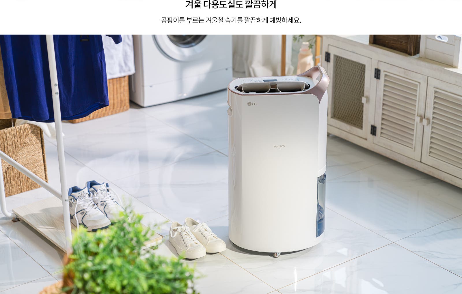 겨울 다용도실도 깔끔하게. 곰팡이를 부르는 겨울철 습기를 깔끔하게 예방하세요. 흰색 LG 휘센 제습기가 바닥에 놓여 있으며, 주변에는 운동화와 빨래 건조대가 있습니다. 배경에는 세탁기와 수납장이 보입니다. 밝은 타일 바닥과 식물이 함께 어우러져 깔끔한 분위기를 연출합니다.
