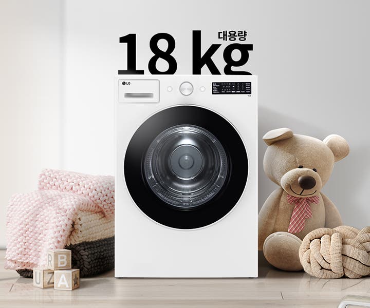 대용량 18kg 세탁기가 놓여 있으며, 주변에는 큰 곰 인형과 분홍색 담요가 놓여 있다. 바닥에는 R, B, U, A가 적힌 나무 블록이 있다. 세탁기 위쪽에는 18kg 대용량이라는 글자가 있다. 배경에는 간단한 디자인의 그림이 걸려 있다.