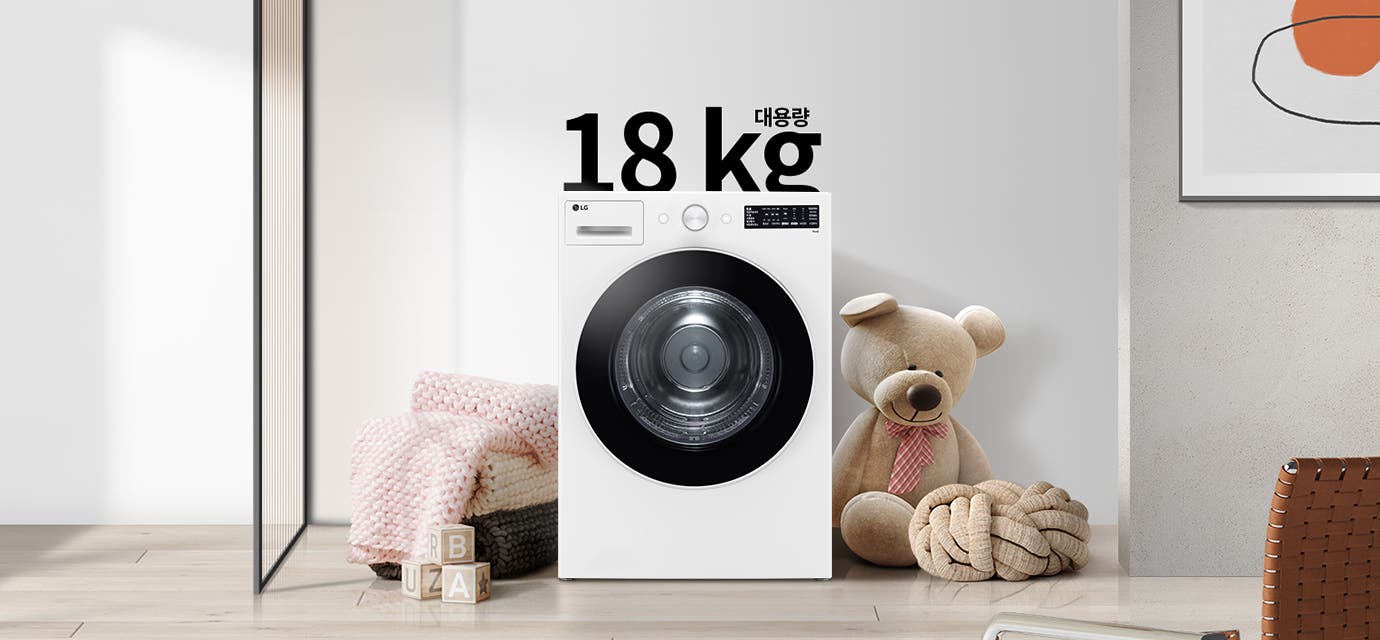 대용량 18kg 세탁기가 놓여 있으며, 주변에는 큰 곰 인형과 분홍색 담요가 놓여 있다. 바닥에는 R, B, U, A가 적힌 나무 블록이 있다. 세탁기 위쪽에는 18kg 대용량이라는 글자가 있다. 배경에는 간단한 디자인의 그림이 걸려 있다.