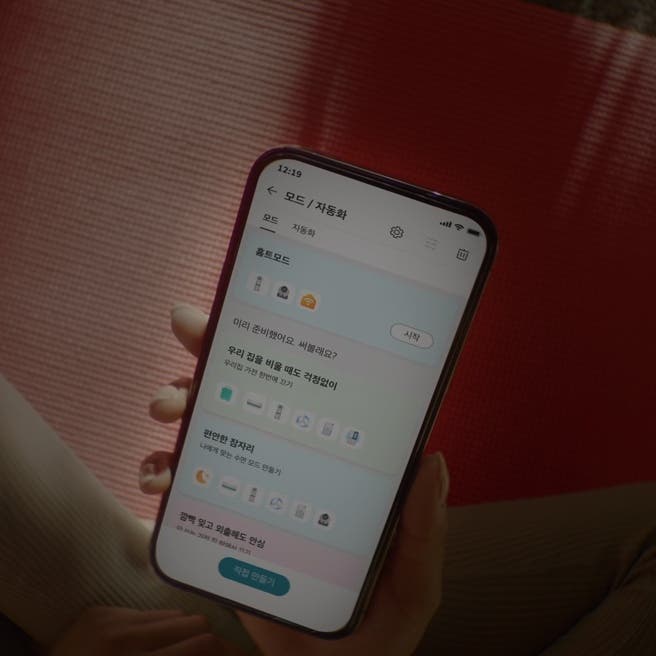 스마트폰 화면에 홈 모드와 관련된 설정 화면이 표시되어 있습니다. 화면 상단에는 모드 / 자동화라는 제목이 있으며, 그 아래에 홈 모드가 선택되어 있습니다. 미리 준비했어요. 써볼래요?라는 문구와 함께 시작 버튼이 보입니다. 그 아래에는 우리 집을 비울 때도 걱정없이 우리집 가전 한번에 끄기라는 문구와 함께 여러 아이콘이 나열되어 있습니다. 편안한 잠자리 나에게 맞는 수면 모드 만들기라는 문구와 함께 여러 아이콘이 나열되어 있습니다. 깜빡 잊고 외출해도 안심이라는 항목이 보입니다. 화면 하단에는 직접 만들기라는 버튼이 있습니다.