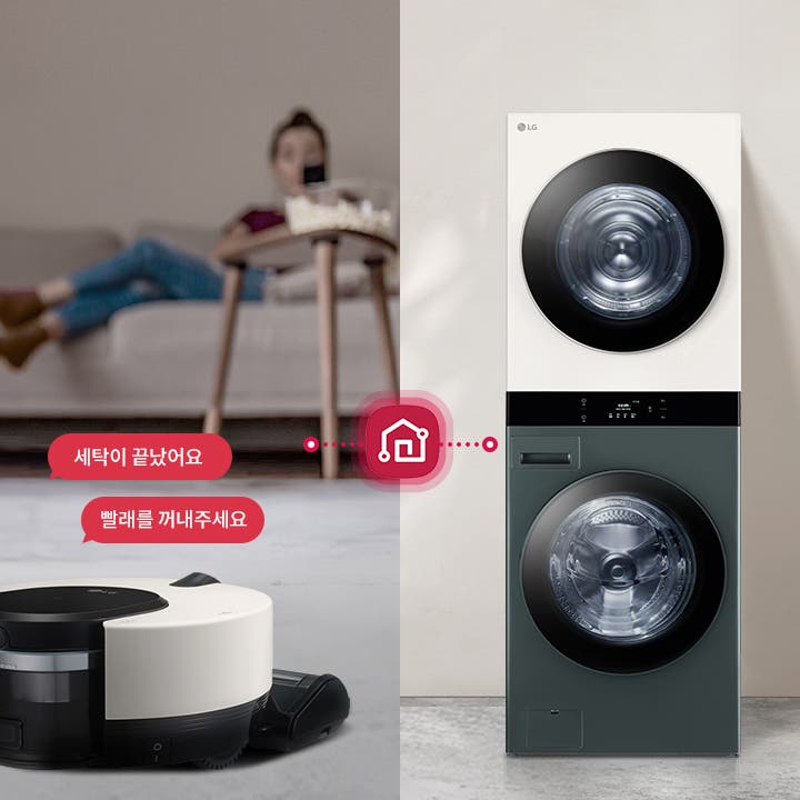 세탁기와 건조기가 위아래로 합쳐진 워시타워의 모습이 보입니다. 소파에 앉아 있는 사람이 있는 다른 공간에 로봇 청소기가 있습니다. 로봇 청소기 위에는 세탁이 끝났어요와 빨래를 꺼내주세요라는 텍스트가 빨간 말풍선 안에 표시되어 있습니다. 로봇 청소기와 워시타워는 빨간색 점선과 ThinQ 아이콘으로 연결되어 있습니다.