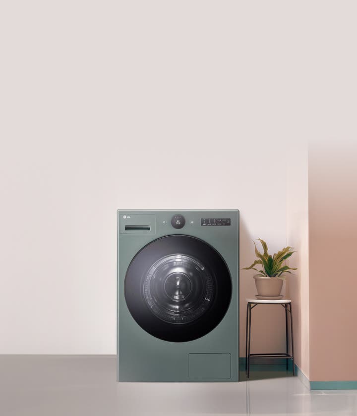 녹색 LG 세탁기가 실내에 배치되어 있으며, 옆의 화분 스탠드에는 녹색 식물이 놓여 있습니다.