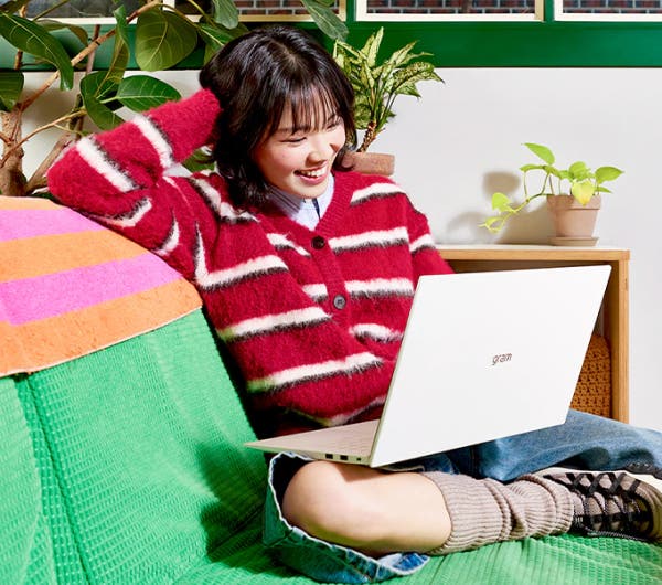야외에서 두 명의 젊은 외국인이 흰색 gram 노트북을 들고 화면을 보며 밝게 웃고 있습니다.