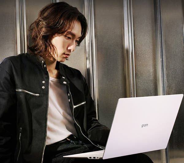 한 남성이 카페에서 노트북을 사용하고 있는 모습으로, 노트북 화면에는 그래픽 디자인 작업 화면이 보입니다.