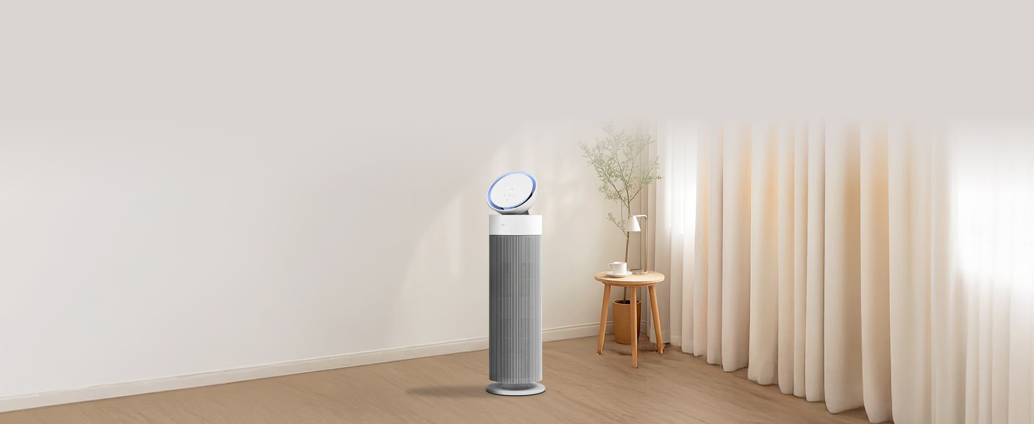 밝고 현대적인 거실에서 LG 퓨리케어 오브제컬렉션 에어로부스터가 중앙에 위치하며, 세련된 원통형 디자인과 상단의 기울어진 원반형 디스플레이가 특징입니다. 옆에는 화분으로 장식되어 있고, 뒤로는 창문이 햇빛을 받아 밝은 분위기를 조성합니다. 전체적으로 미니멀하고 깨끗한 공간을 연출합니다.
