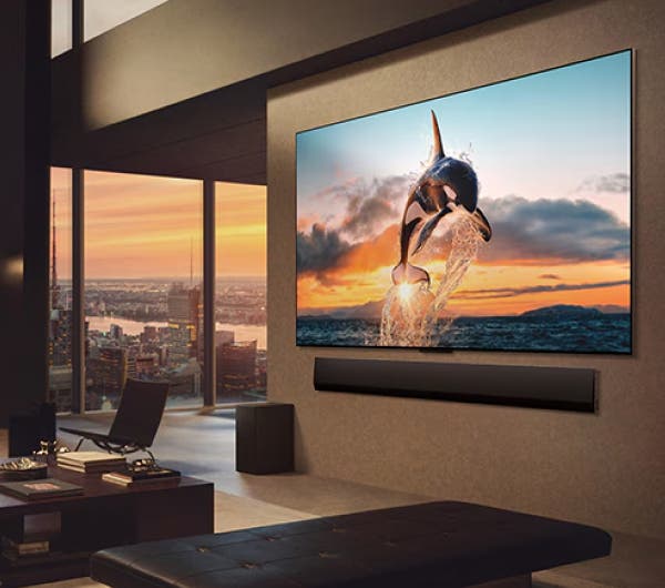 도시 풍경을 감상할 수 있는 넓은 거실. LG OLED TV는 LG 사운드바가 있는 벽에 장착되어 있습니다. TV의 원월 디자인으로 벽에 플러시 핏을 맞추고 공간과 잘 어우러집니다. 제로 커넥트 박스는 보이지만 숨겨져 있습니다.