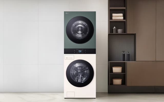실내에 설치된 LG 워시타워로, 상단에는 녹색 건조기, 하단에는 흰색 세탁기가 세로로 구성되어 있습니다. 오른쪽에는 선반과 수납장이 있는 모듈형 선반이 배치되어 있으며, 양쪽 벽은 흰색 타일로 마감되어 있습니다.