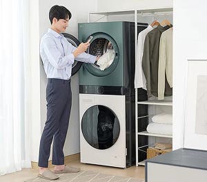 세탁기와 건조기가 세로로 설치된 공간에서 남성이 세탁물을 넣는 모습