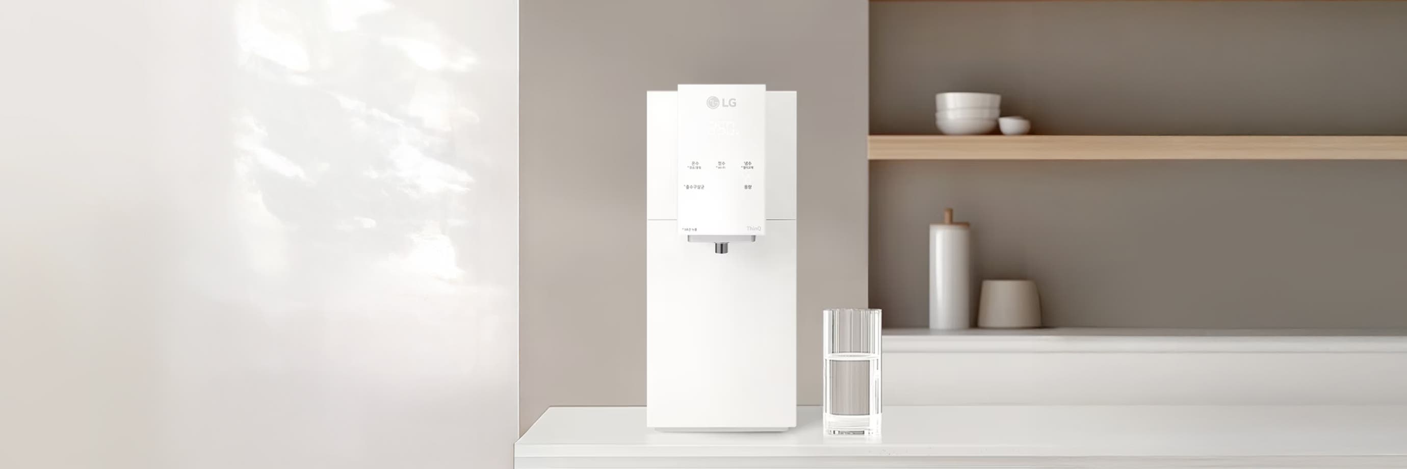 산뜻한 톤의 주방 공간에 화이트 컬러의 LG 퓨리케어 오브제컬렉션 정수기가 놓여 있어요. 옆에는 유리컵과 미니멀한 소품들이 정돈되어 배치되어, 전체적으로 깔끔하고 부드러운 분위기를 만들어 줍니다.