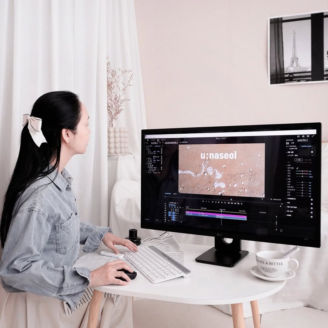 LG 스마트모니터를 사용해 영상 편집 프로그램을 실행한 모습이다. 여성이 키보드와 마우스를 활용해 작업을 진행하고 있으며, 책상 위에는 커피잔과 다양한 작업 도구들이 놓여 있다.