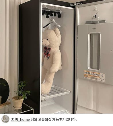 LG 스타일러 오브제컬렉션의 문이 열려 내부가 보이는 모습. 내부에는 큰 곰 인형이 옷걸이에 걸려 있고, 하단에는 액세서리 보관용 선반이 배치되어 있음. 깔끔하고 넉넉한 내부 공간이 돋보이며, 하단에는 '지비_home 님의 오늘의집 제품후기입니다.'라는 텍스트가 포함되어 있음. 