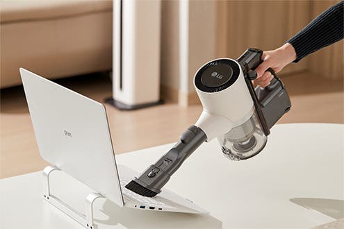 LG 코드제로 A9S 오브제컬렉션으로 노트북 주변을 청소하는 모습. 핸디형 청소기를 사용하여 간편하게 먼지를 제거하는 장면.
