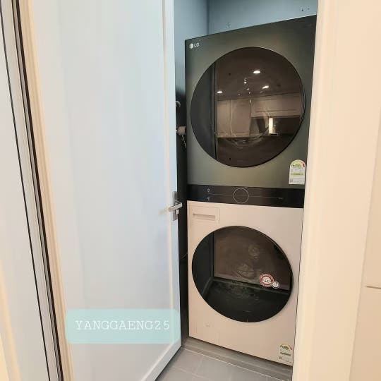 세탁실 문을 열었을 때 내부에 세탁기와 건조기가 나란히 배치되어 있으며, 벽면에는 수도 배관과 가스 배관이 정리되어 있음