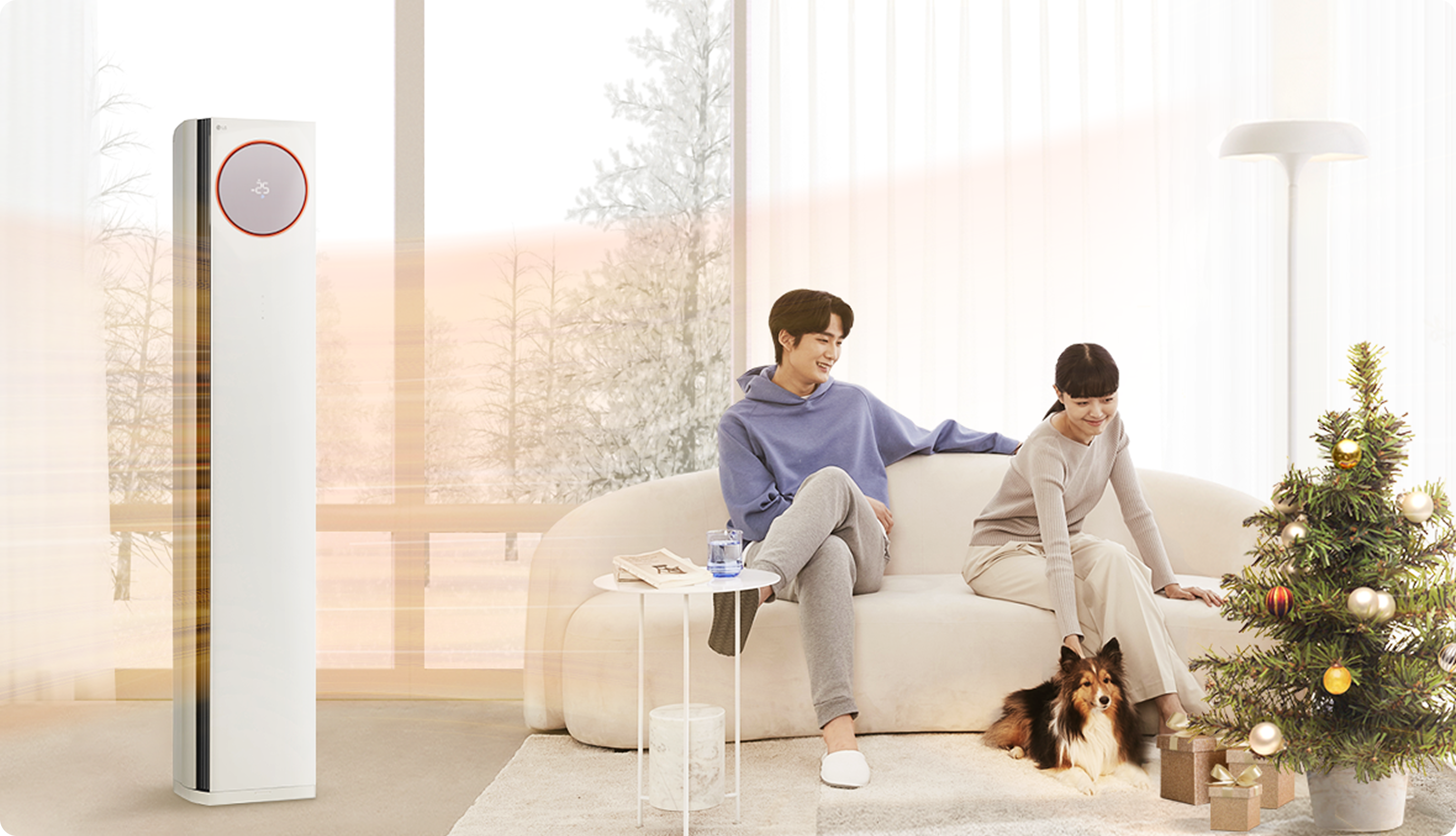 눈 덮인 겨울 배경의 거실에서 남성과 여성이 반려견과 함께 소파에 앉아 있다. 크리스마스트리가 놓여 있고, LG 휘센 에어컨이 따뜻한 바람을 내보내며 실내를 포근하게 데우는 장면.