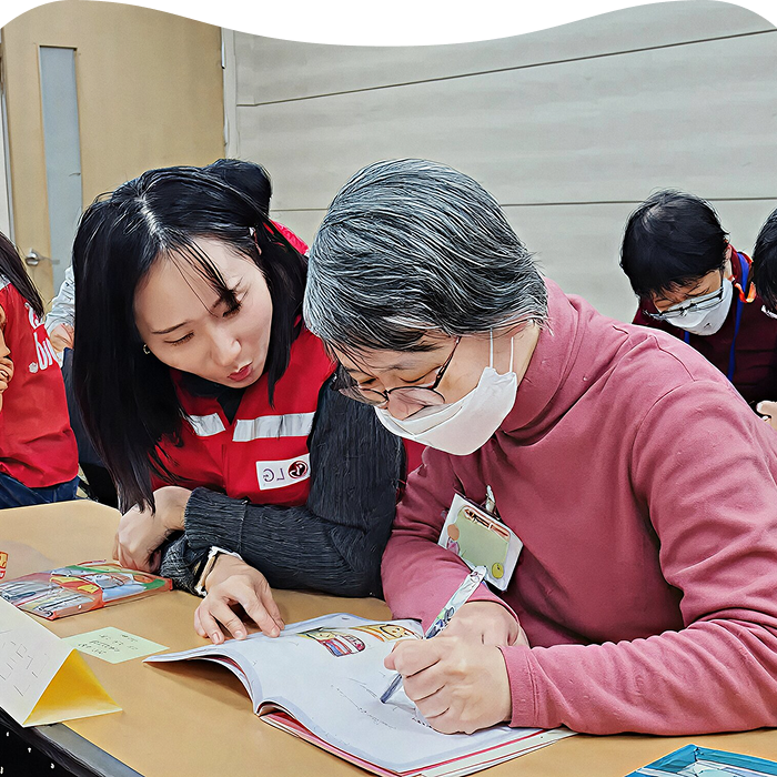 LG School 프로그램 현장에서 LG 관계자가 복지관 어르신과 함께 쉬운 읽기 교재를 보며 가전 사용 방법을 안내하고 학습을 돕는 모습