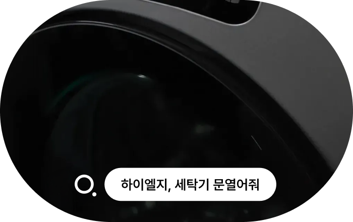 LG 세탁기 AI 음성 인식 기능 이미지입니다. LG 세탁기 상단 근접 촬영 화면에 음성 인식 아이콘과 함께 '하이엘지, 세탁기 문열어줘' 텍스트가 표시되어 있으며, 세탁기 문이 열린 모습입니다.