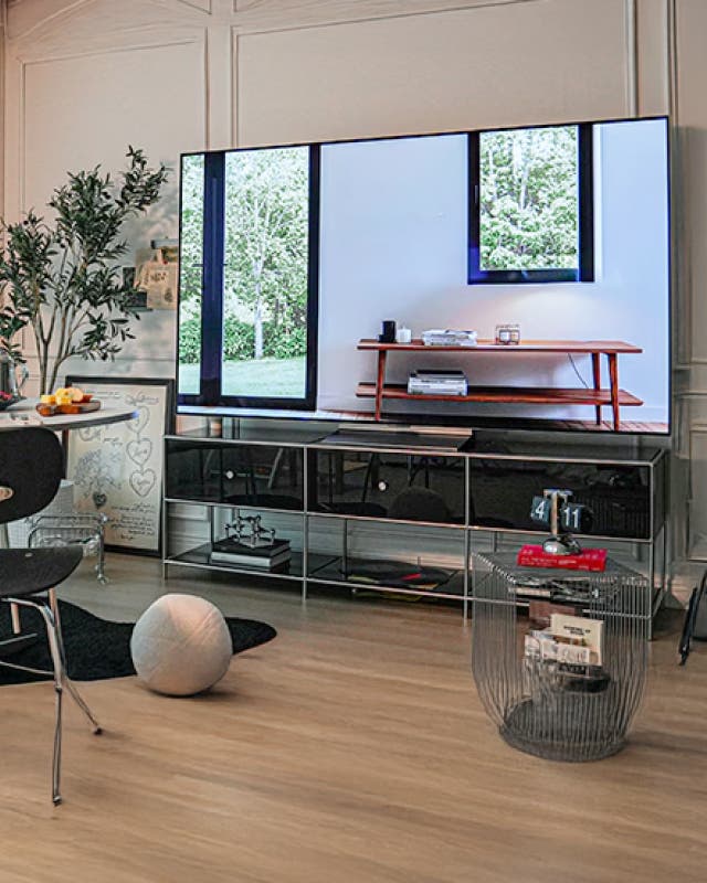 거실에 설치된 LG OLED evo TV가 켜져 있으며, 화면에 푸른 나무와 창문 풍경이 비치고 있다. TV 주변에는 테이블과 의자, 소품들이 배치되어 있다